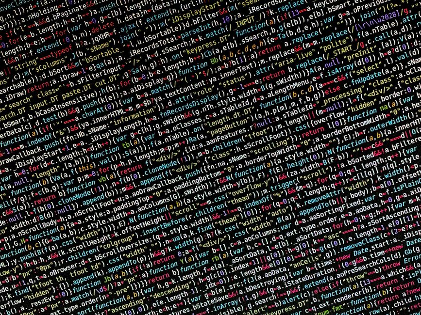 Close-up view of a computer monitor displaying a coding script with various lines of text in multiple colors including white, green, red, and purple, indicating different code elements and variables. 